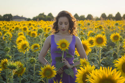 Portrait of young woman standing against sunflower field