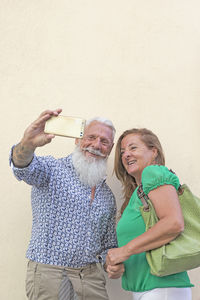 Mature couple taking selfie while standing against beige background