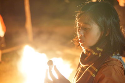 Close-up of woman holding marshmallow against campfire at night