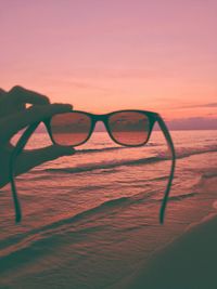 Close-up of sunglasses against sea during sunset