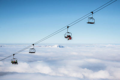 Ski lifts above cloudscape against clear sky