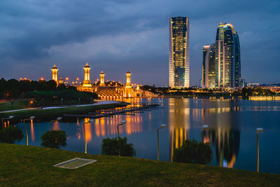 Illuminated buildings by river against sky in city