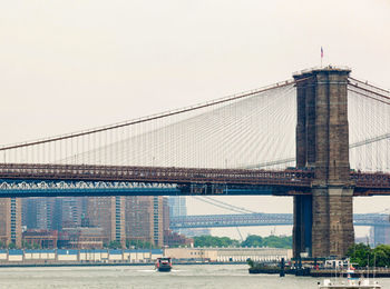 Low angle view of brooklyn bridge over river in city against clear sky