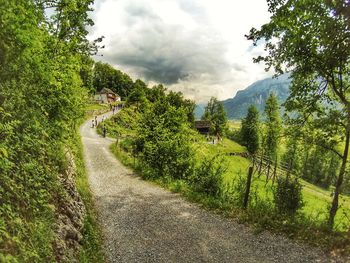 Footpath by road against cloudy sky