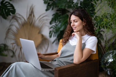 Woman freelancer working on laptop surrounded by exotic houseplants in home garden. cozy workplace.