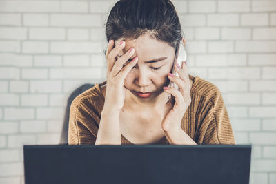 Portrait of young woman using phone while sitting on wall