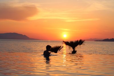 Silhouette people in sea against sky during sunset