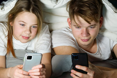 Sibling using mobile phone lying on bed at home