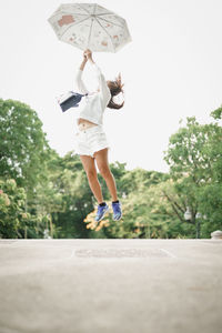 Rear view of woman jumping against trees