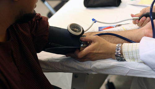 Cropped image of doctor examining patient arm with blood pressure gauge and stethoscope in medical clinic