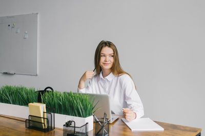 A cute girl is sitting at a desk in the office working with a laptop and notepad and looking away