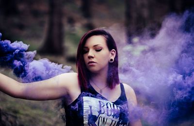 Beautiful young woman by purple smoke against trees