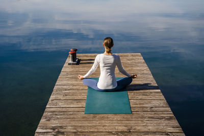 Woman meditating at jetty on sunny day