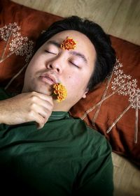 Portrait of young man lying down with yellow flower on forehead and holding yellow, marigold flower.