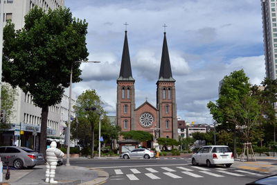 Cars on road by buildings against sky in city