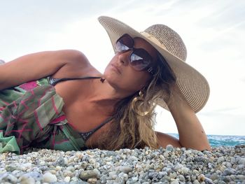 Woman wearing sunglasses lying at beach against sky