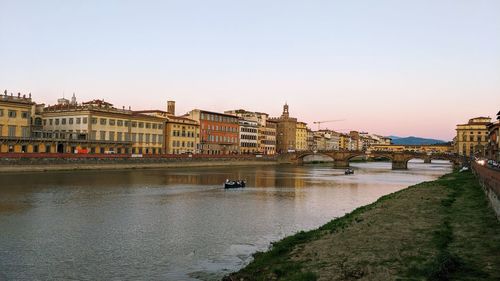 Bridge over river by buildings against clear sky