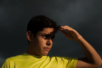 Thoughtful teenage boy shielding eyes against storm clouds