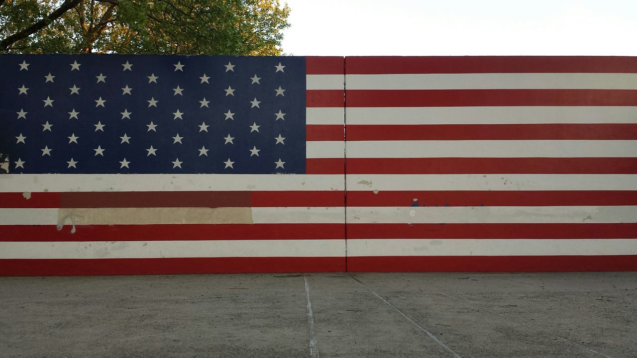 patriotism, identity, flag, american flag, national flag, striped, culture, red, white color, pride, wind, star shape, clear sky, low angle view, outdoors, day, road marking, sky, building exterior, no people