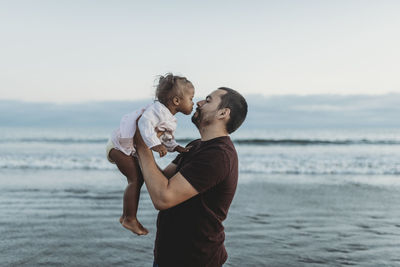 Dad and daughter playing in the ocean at dusk