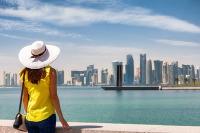 Rear view of woman wearing hat while standing against cityscape