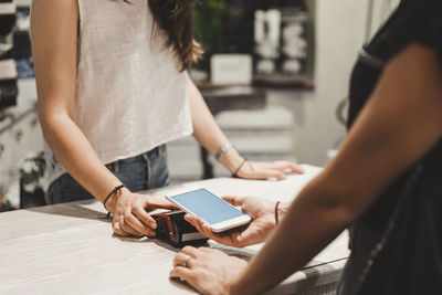 Midsection of female customer making contactless payment with smart phone to owner in clothing store