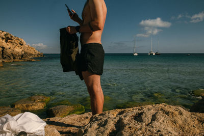 Man standing on rock in sea against sky