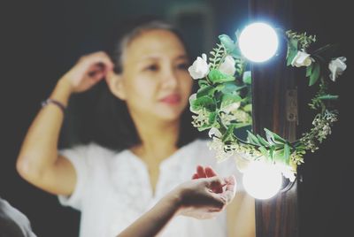 Woman touching illuminated decoration while reflecting on mirror