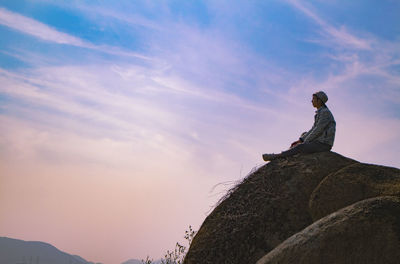 Man sitting on rock against sunset