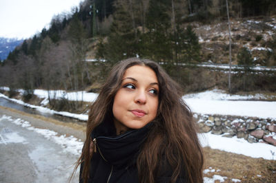 Young woman looking away while standing on road during winter