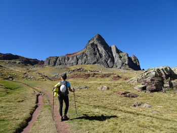 Rear view of man walking on mountain against clear blue sky