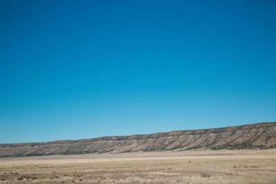 Scenic view of arid landscape against clear blue sky during sunny day