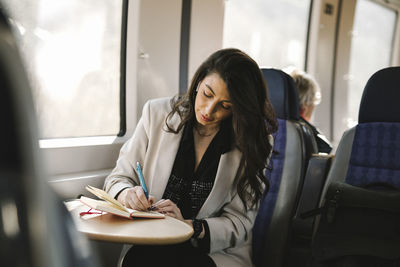 Businesswoman writing in diary while sitting by train window