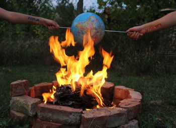 Cropped hands burning globe at fire pit in backyard