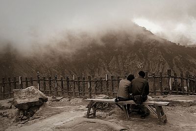 Rear view of man sitting on mountain during foggy weather