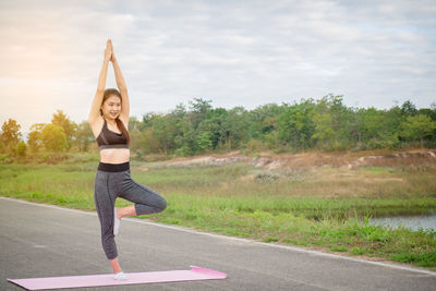 Full length of young woman exercising on road against sky