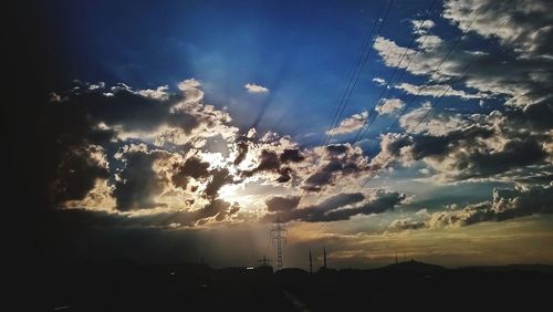 Low angle view of silhouette electricity pylon against dramatic sky