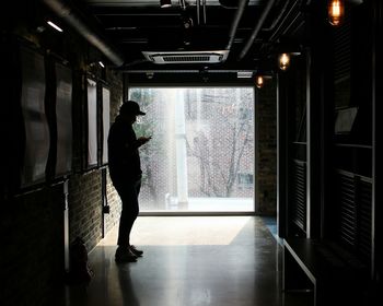 Silhouette man using mobile phone while standing in corridor