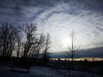 Silhouette bare trees on field against sky during winter