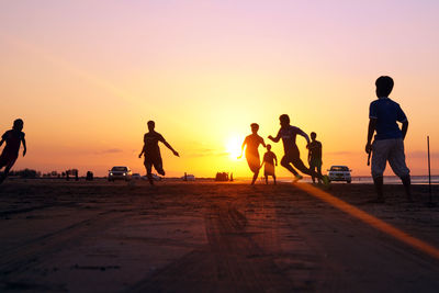 People playing soccer on beach against sky during sunset