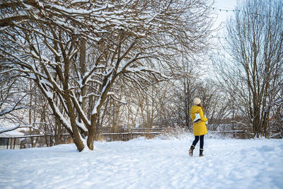 Young woman in yellow jacket with ice skates walking through snowy park