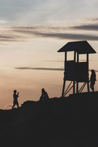 Silhouette people on beach against sky during sunset