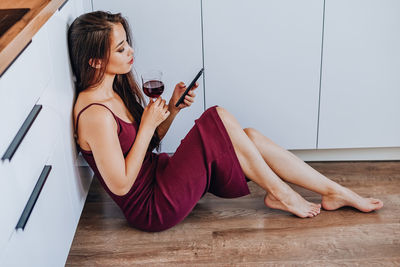 Young woman using phone while sitting on wooden floor