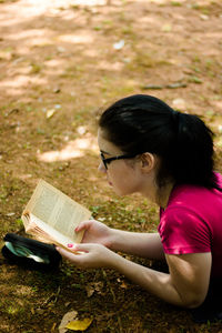 High angle view of young woman reading book while lying on field at park