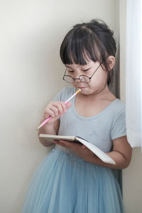 Midsection of woman holding eyeglasses against wall