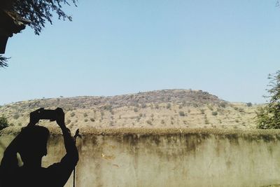 Man photographing on mountain against clear sky