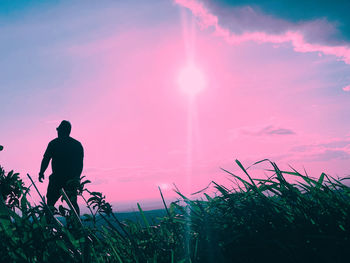 Rear view of silhouette man standing on field against sky during sunset