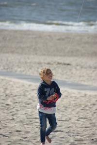 Girl flying kite while standing on sand at beach