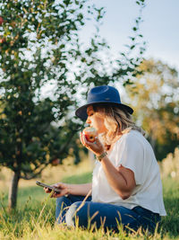 Side view of woman holding mobile phone while sitting on field