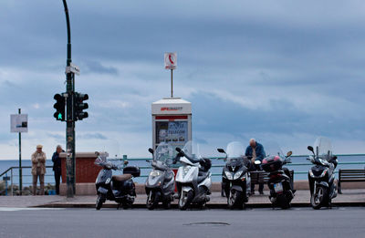 Motor scooters parked on roadside against cloudy sky